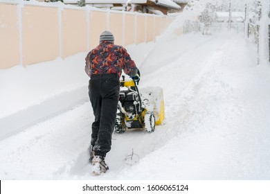 man operating snow blower to remove snow on driveway. Man using a snowblower. A man cleans snow from sidewalks with snowblower