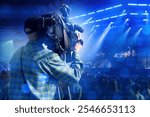 Man operator films concert on camera. Videographer guy back to display. Man director points camera at stage. Specialist is broadcasting video from nightclub. Videographer holds professional camera