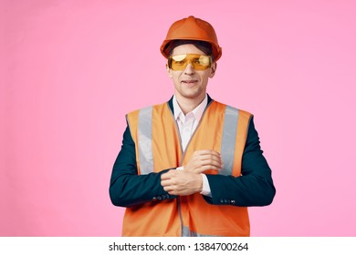 a man in an orange helmet and a reflective vest on a pink background, yellow sunglasses and a blue jacket                            - Powered by Shutterstock