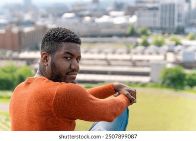 Man in an Orange Sweater Gazes Over City Skyline From Grassy Hill During Bright Day - Powered by Shutterstock