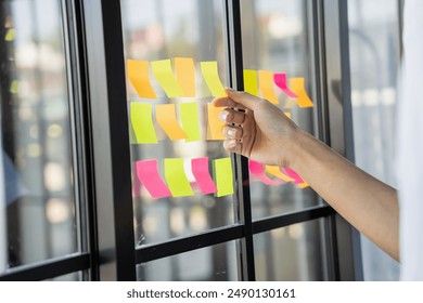 Man organizing project tasks Colorful sticky notes on glass of meeting room.