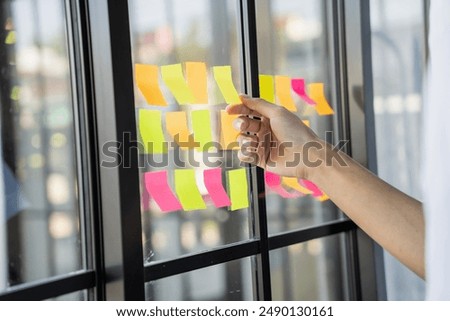 Man organizing project tasks Colorful sticky notes on glass of meeting room.
