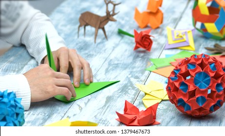 Man at origami folding lesson. Collection of beautiful origami figurines on wooden table. Traditional origami paper folding. - Powered by Shutterstock - Get 15% off with code: PIKWIZARD15