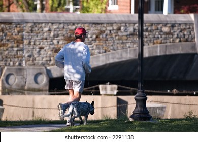 Man Out For An Early Morning Jog In The Park With Dog.