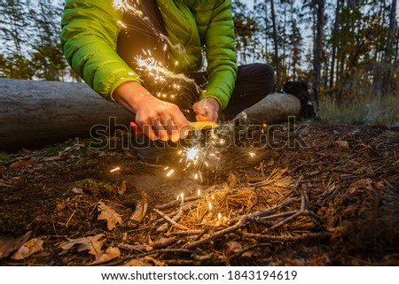 Man outdoors makeing fire by flint. Front view. Flying sparks.