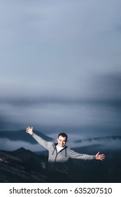Man Outdoors on the Roof of the Building with Hands Raised with Cloudy Hills on Background