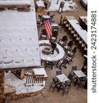 A man outside preparing a fire pit for the ski crowds at a Beaver Creek Resort with snow and chairs all around and an American Flag hanging above him as he works hard in the service industry Colorado