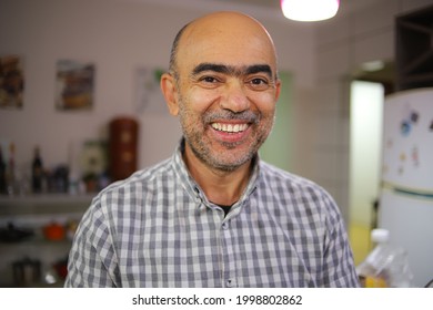 Man Over 50 Years Old, Smiling, In A Plaid Shirt, Inside A Kitchen.