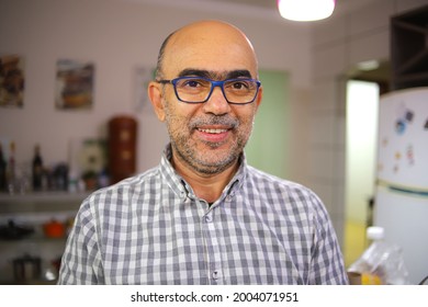 Man Over 50 Years Old, Smiling, In A Plaid Shirt, Inside A Kitchen.