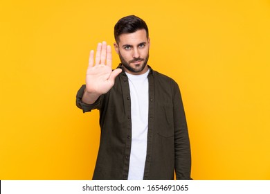 Man over isolated yellow background making stop gesture with her hand - Powered by Shutterstock