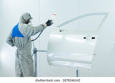 Man in overalls paints the car door using factory technology. Man in a mask, respirator. spray painting of car parts. car repair shop. white background. black mittens