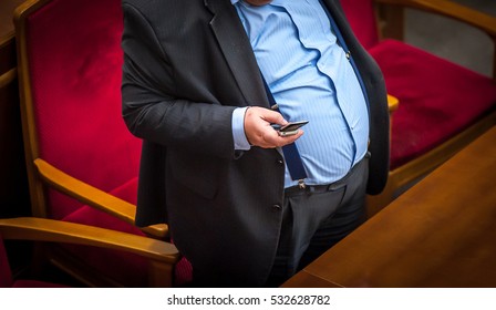 man with overweight. symbolic photo for beer belly, unsuccessful dieting and eating the wrong foods. Weight loss concept. Tight shirt. a man in a suit, suspenders and tie near chair. hands in pockets