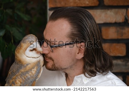 Man with owl at home. Unusual pets and human animal friendship relationships. Wild bird on hand glove tenderness and love.