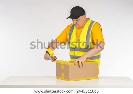 Man packer at work. Warehouse worker seals box with tape. Dispenser with tape in hands man. Packer guy is near table. Businessman is preparing parcel for shipment. Packer of goods from online store