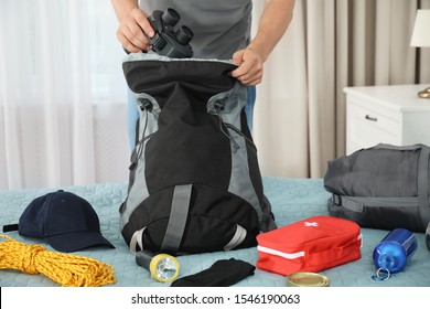 Man Packing Different Camping Equipment Into Backpack At Home, Closeup