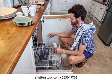 Man Packing Dirty Dishes Into Dishwashing Machine In Home Kitchen