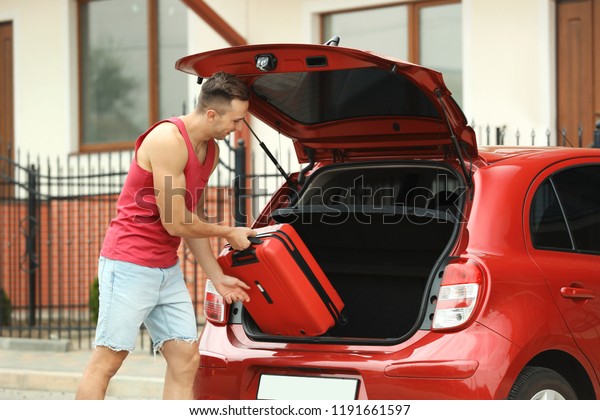 Man\
packing suitcase into car trunk on city\
street