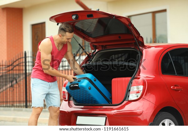 Man\
packing suitcase into car trunk on city\
street