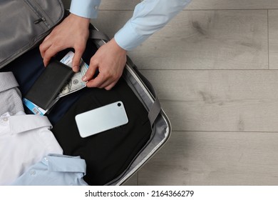 Man Packing Suitcase On Wooden Floor, Top View With Space For Text. Business Trip Planning