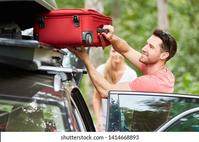 Man Packs Suitcases In The Roof Box On The Car Before Traveling On Vacation