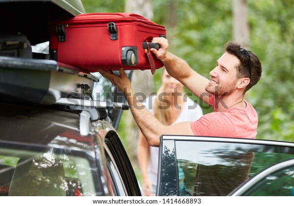 Man packs suitcases in the roof box on the car\
before traveling on\
vacation