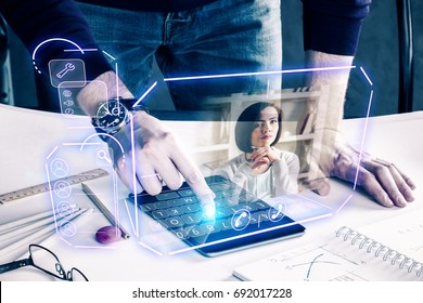 Man with pad leaning on desk at workplace and communicating with young woman via abstract futuristic screen hologram. Concept of network, communication, family, technology, augmented reality 
 - Powered by Shutterstock