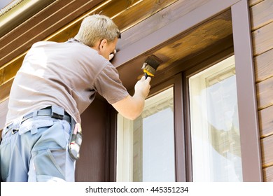 man with paintbrush painting wooden house exterior