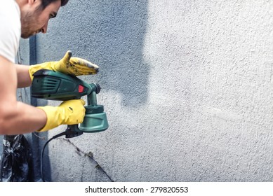 Man painting a grey wall, renovating exterior walls of new house