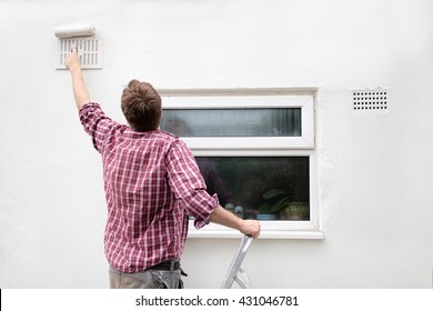 Man Painting House Wall On Stepladder With Paint Roller. DIY Home Improvement.