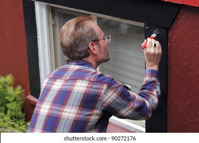 Man Painting House Window Trim With Black Paint Outdoors In The Day.