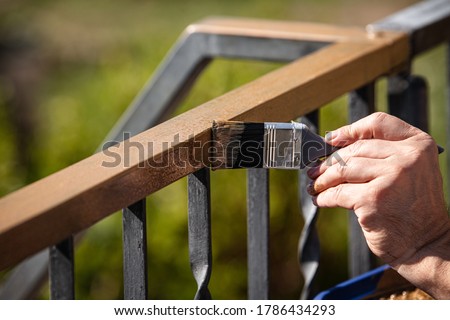 a man is painting a metal railing with copper varnish, close up outdoor shot