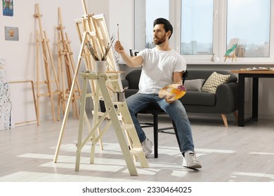 Man painting in studio. Using easel to hold canvas - Powered by Shutterstock