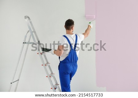 Man painting wall with light pink dye indoors, back view