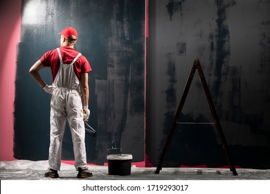 Man Painting A Wall. Painter In Red Overall Painting Wall In Black Color