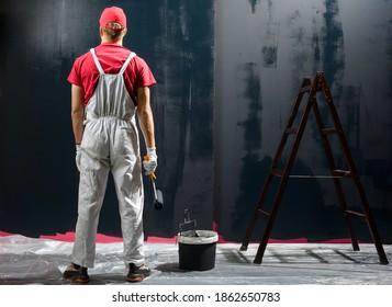 Man Painting A Wall. Painter In Red Overall Painting Wall In Black Color