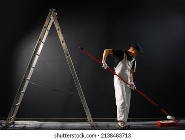 Man Painting A Wall. Painter In Red Overall Painting Wall In Black Color