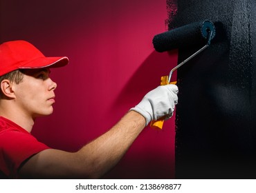 Man Painting A Wall. Painter In Red Overall Painting Wall In Black Color