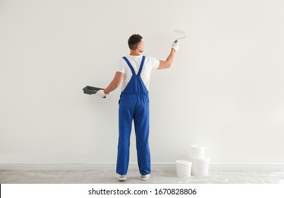 Man painting wall with white dye indoors, back view