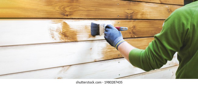 Man Painting Wood House Exterior Siding With Brown Protective Paint. Banner Copy Space