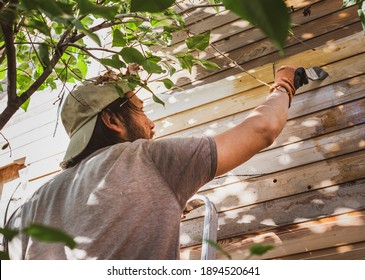 Man Painting Wooden Wall Of House Outdoors