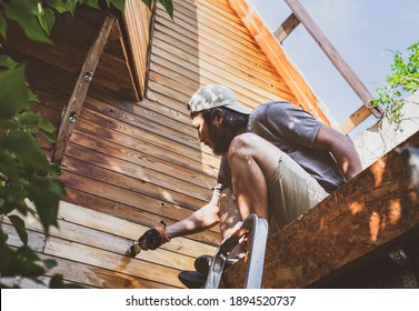 Man Painting Wooden Wall Of House Outdoors