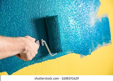 Man painting yellow wall with blue dye, closeup