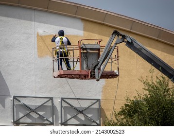 Man Painting A Yellow Wall White Using A Paint Sprayer While Standiong On A Manlift 