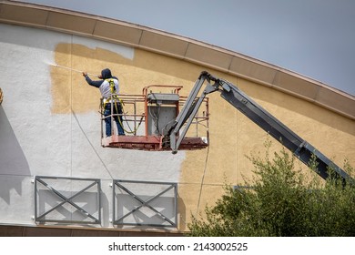 Man Painting A Yellow Wall White Using A Paint Sprayer While Standiong On A Manlift 