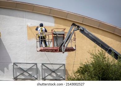 Man Painting A Yellow Wall White Using A Paint Sprayer While Standiong On A Manlift 