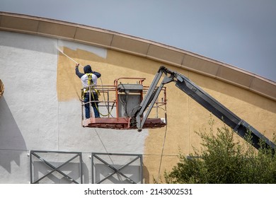 Man Painting A Yellow Wall White Using A Paint Sprayer While Standiong On A Manlift 