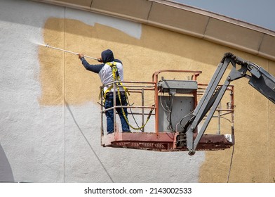 Man Painting A Yellow Wall White Using A Paint Sprayer While Standiong On A Manlift 