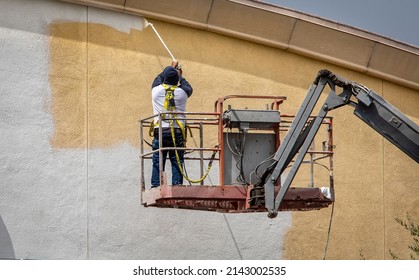 Man Painting A Yellow Wall White Using A Paint Sprayer While Standiong On A Manlift 