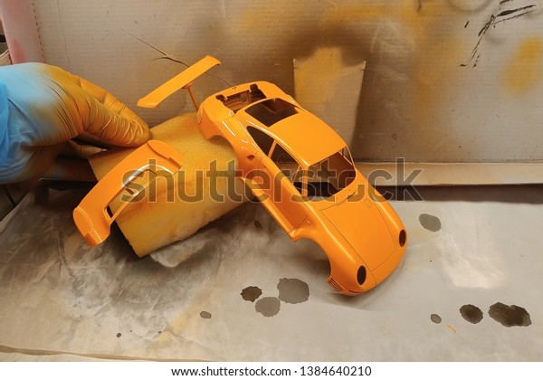 A man paints a scale model\
car. Paint the spoiler, trunk lid and toy body in a bright orange\
color.