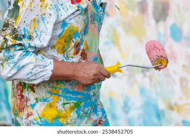 A man in a paint-splattered apron holding a paint roller. Concept of creativity and artistic expression - Powered by Shutterstock